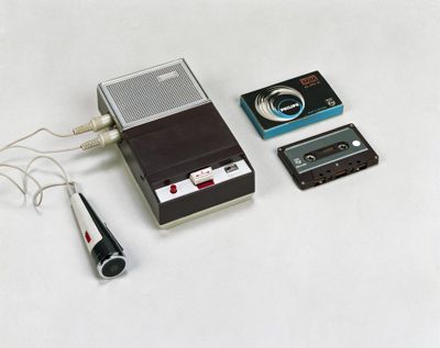 Early Philips cassette recorder with microphone and cassette alongside original packaging and media
