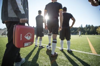 Person håller Philips-AED-väska på fotbollsplan med spelare