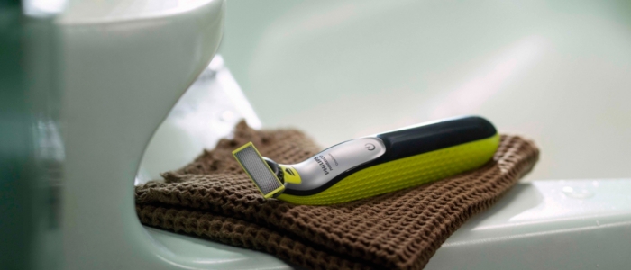 Ready to be used after exfoliating beards, the OneBlade shaver sits on a towel next to a sink.