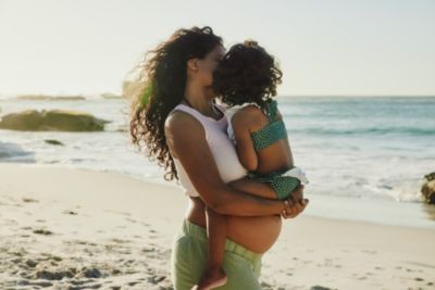 Pregnant woman holding a young child while standing on a beach