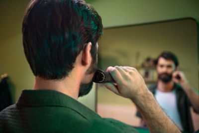 Een man kijkt in de spiegel terwijl hij zijn dikke baard scheert met de Philips OneBlade.