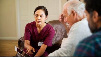 Healthcare worker showing information on a tablet to an elderly man at home