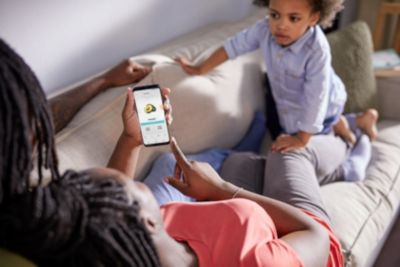 A person lying on a couch surfing on a smartphone, with a young boy sitting next to her