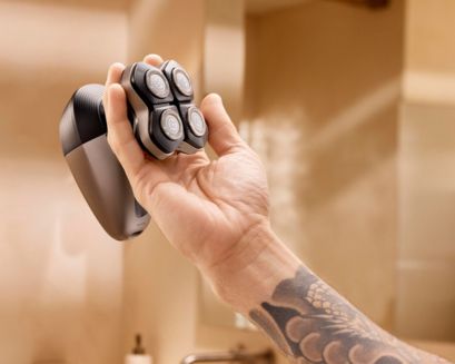 Philips head shaver held in tattooed hand in bathroom