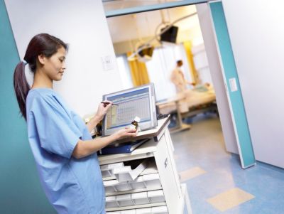 Nurse updating electronic medical records on a computer in hospital corridor