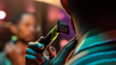 Een man trimt zijn baard met een Philips Norelco baardtrimmer terwijl hij in een wazige spiegel kijkt.