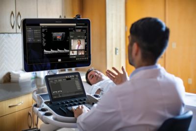 Clinician conducts bedside scan with Philips ultrasound system featuring real-time remote consultation while patient lies on examination table
