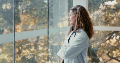 Doctor standing by hospital window looking outside with arms crossed