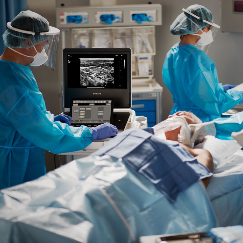 Patient in anesthesia setting with clinicians consulting mobile ultrasound system