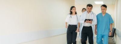 Tenaga medis berjalan di koridor rumah sakit sambil mendiskusikan perawatan pasien menggunakan tablet