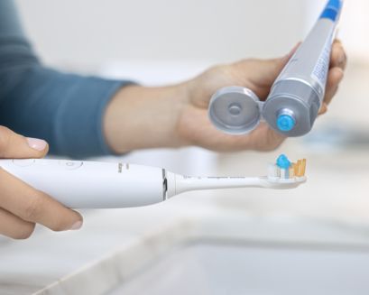Toothpaste being put on Sonicare power toothbrush.
