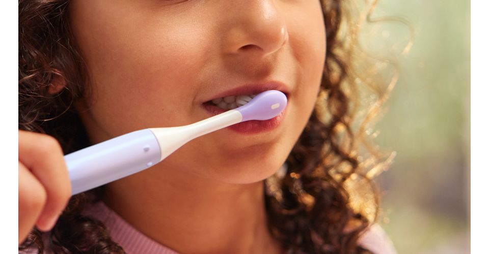 Een jong kind met bruin krullend haar poetst haar tanden met de Philips Sonicare for Kids tandenborstel.