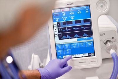 Clinician adjusting settings on Philips Respironics V60 Plus ventilator in hospital care environment