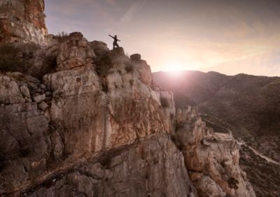 Hiker on Rocky Cliff at Hiker standing on a rugged cliff at sunrise