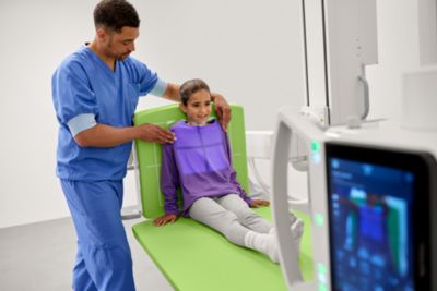 Clinician positions pediatric patient on Philips imaging system table with diagnostic image on monitor
