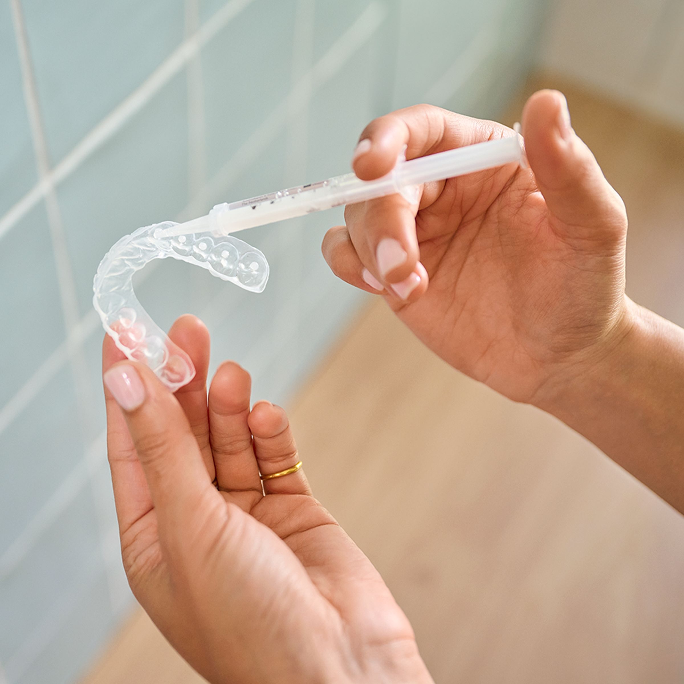Hands applying whitening gel to a whitening tray.