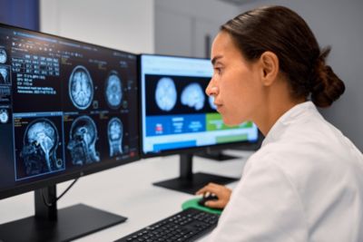 Especialista clínico revisando resonancias magnéticas cerebrales en una estación de trabajo de imagen con doble monitor