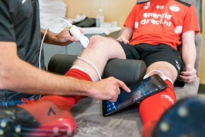 Un clínico utiliza el ecógrafo portátil Philips Lumify con una tableta para evaluar la rodilla de un atleta en un entorno de medicina deportiva