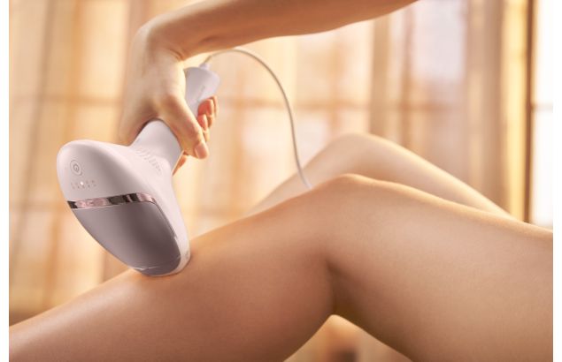 A woman using a grey Philips IPL Lumea machine on her legs.