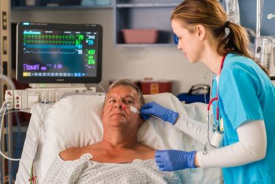 Nurse applying Nasal Alar sensor while monitoring patient in hospital bed