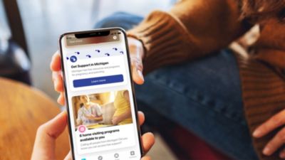 Person holding smartphone displaying Philips Avent Pregnancy+ app with Michigan maternal health resources and home visiting programs.