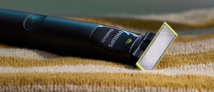A Philips OneBlade shaver sits on top of a striped towel, ready to be used for shaving in the shower.