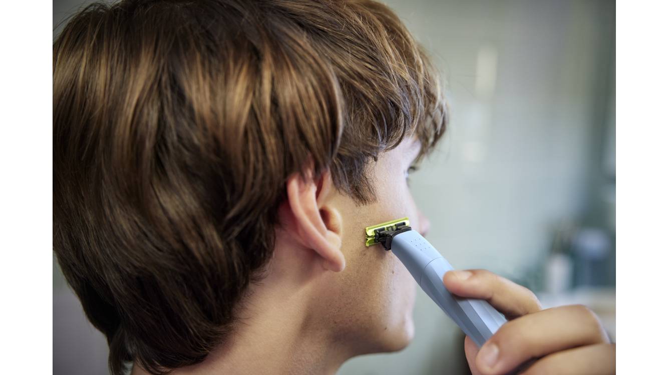 Ein junger Mann schaut von der Kamera weg, während er seine Koteletten mit einem Philips OneBlade rasiert.
