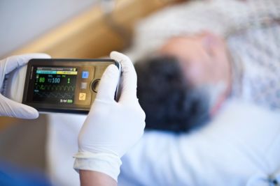 Clinician using Philips IntelliVue patient monitoring device beside patient in bed
