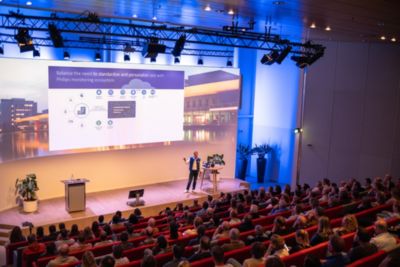 Speaker presenting Philips healthcare technology overview to a seated auditorium audience