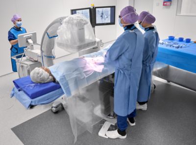 Three clinicians conducting an invasive procedure with imaging guidance.