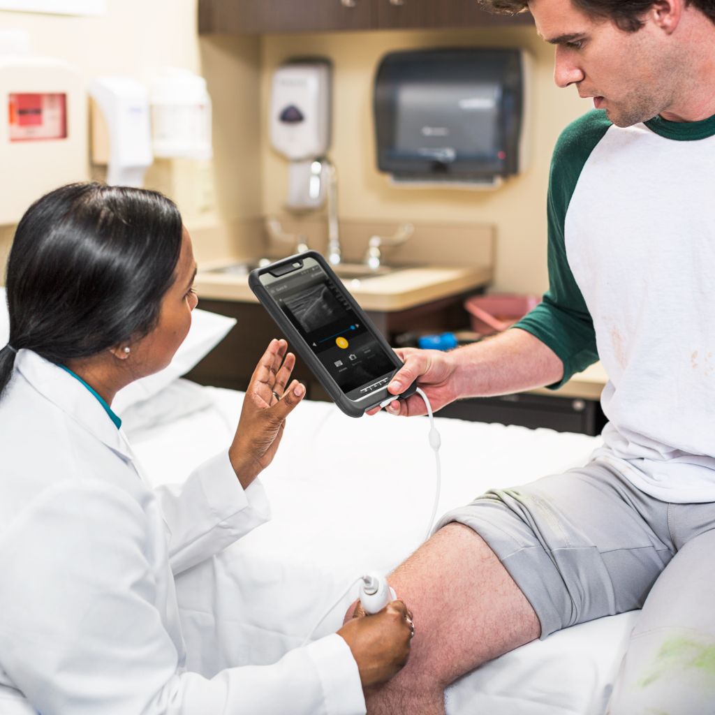Clinician using mobile ultrasound to scan patient knee in clinic setting.