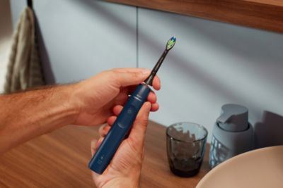 Hand hält eine elektrische Zahnbürste in der Nähe eines Waschbeckens im Badezimmer