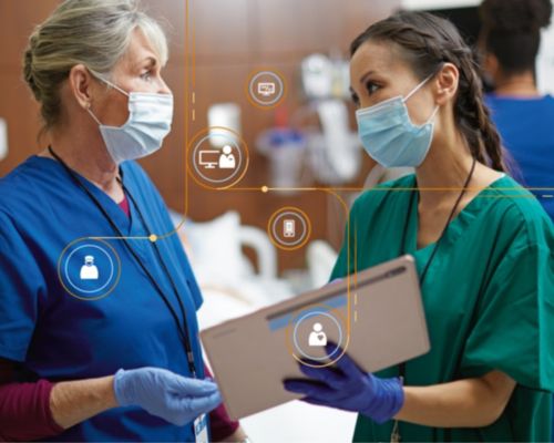 Two nurses conferring in a hospital room at a tablet