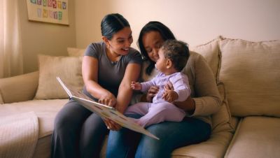 Two adults reading book with baby on couch at home
