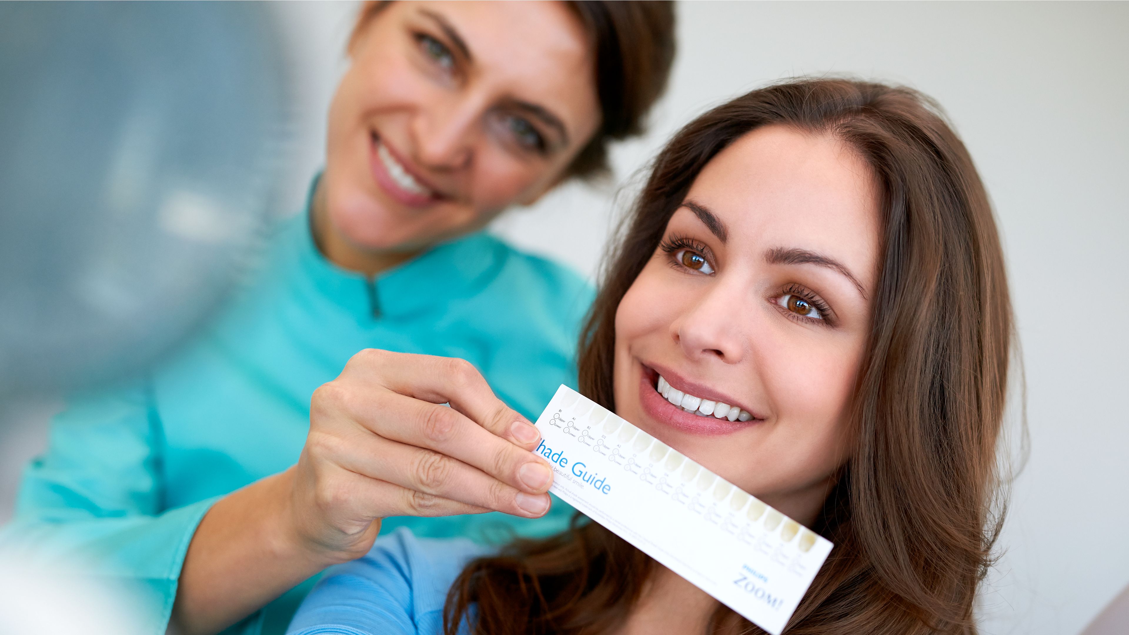 Smiling patient holding a shade guide close to her smile