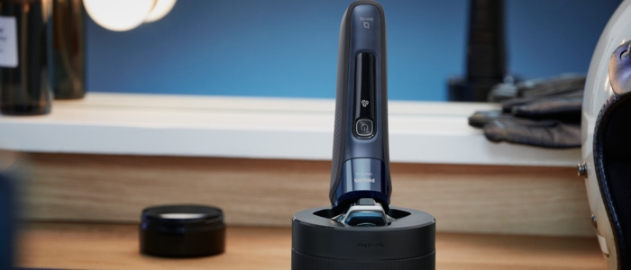 A Philips Quick Clean Pod is cleaning a shaver in a bathroom, next to a bike helmet and a pot of balm.