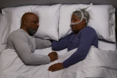 A couple is asleep in bed. The woman is wearing a CPAP mask.