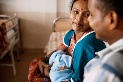Mother holding newborn baby and smiling at partner in hospital room
