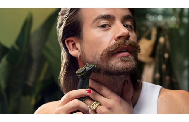 Een jongeman gebruikt een trimmer met een speciaal hulpstuk om een warrige baard te trimmen.
