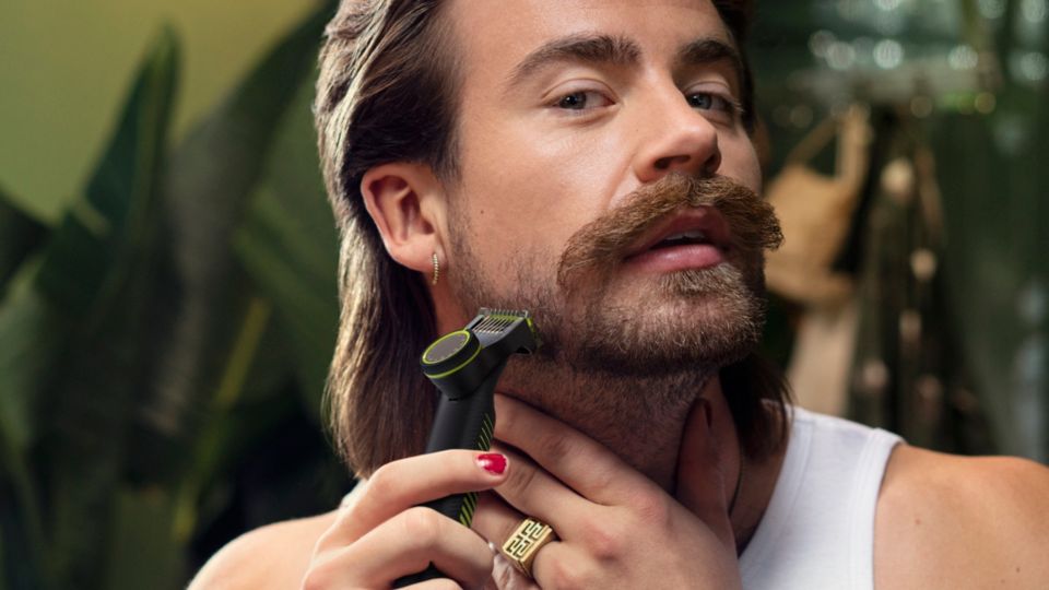 En ung man tittar bort från kameran när han rakar sina polisonger med en Philips OneBlade.