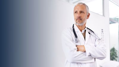 Een zorgprofessional in een witte jas wordt getoond in een lichte klinische omgeving met grote ramen