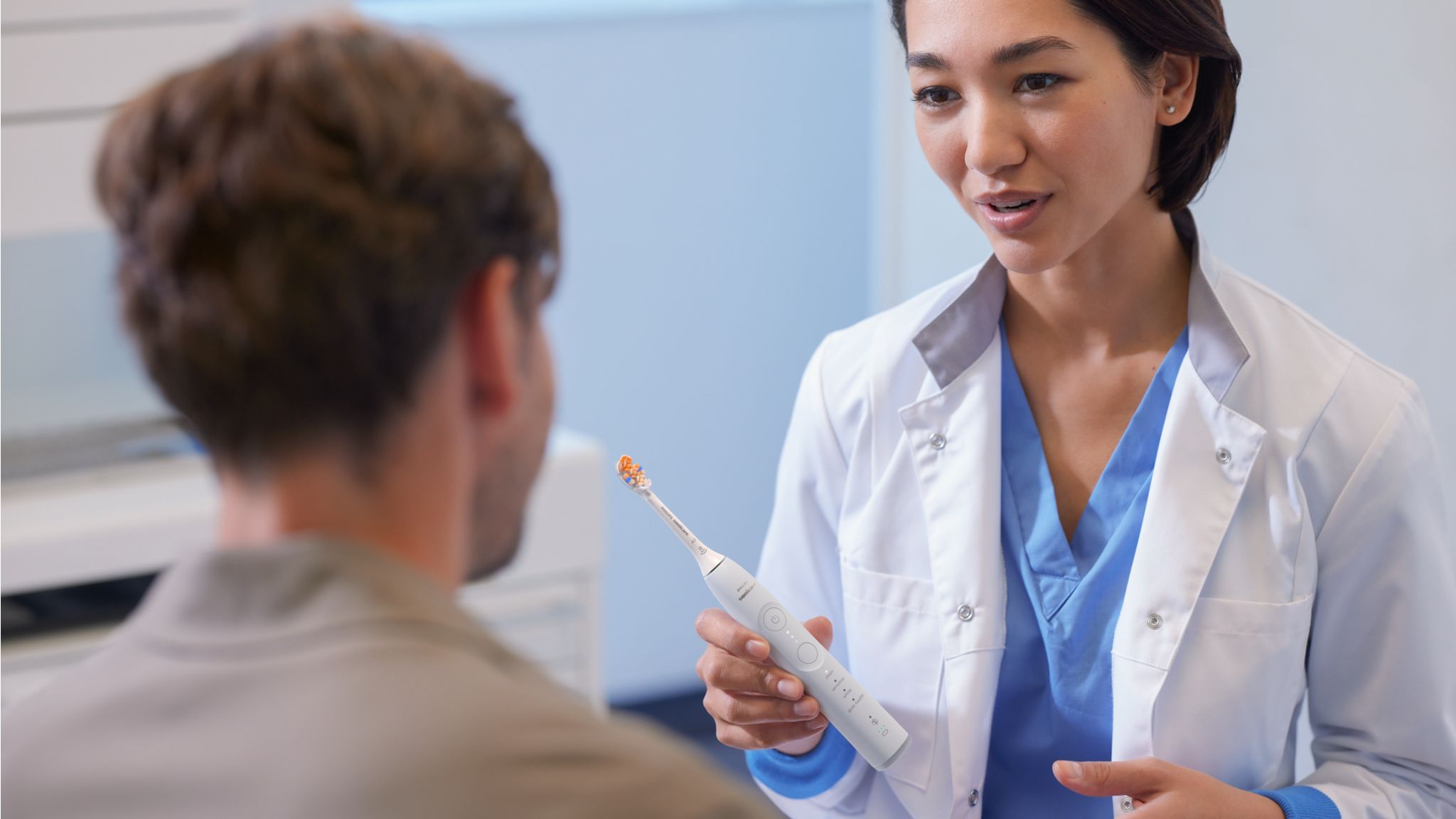 A young dental professional shows a white Philips electric toothbrush to her patient while discussing bleeding gums.