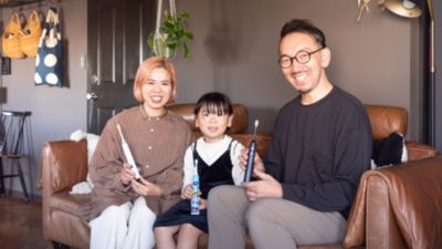 ソファに座り、ソニッケアーの歯ブラシを持った家族