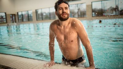 Een shirtloze man met een dikke baard trekt zichzelf uit een binnenzwembad.