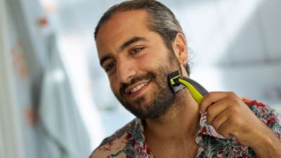 Erwachsener, der den Bart mit einem elektrischen Friseur vor einem Spiegel trimmt