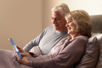 An older couple sits comfortably in bed reviewing sleep therapy data on a mobile device, representing connected care and patient engagement with sleep apnea treatment.
