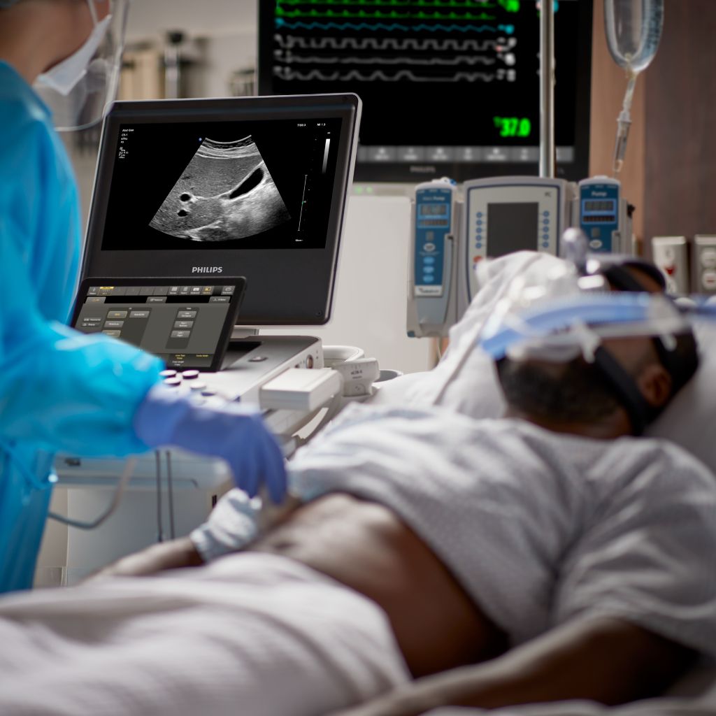 A clinician performs an abdominal ultrasound exam on a patient with a mask on