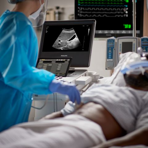 A clinician performs an abdominal ultrasound exam on a patient with a mask on. 
