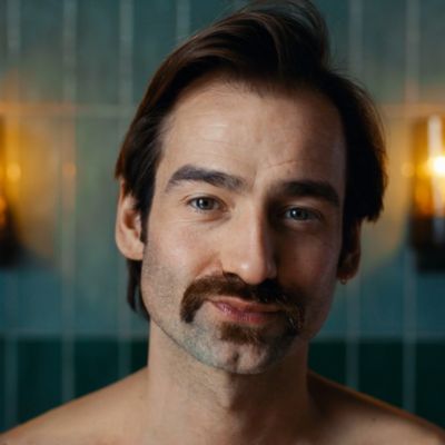 A man with a dark brown beard looks at the camera in a brightly lit room.