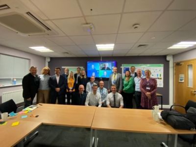 Group of professionals gathered in a meeting room with a video conference screen displaying remote participants